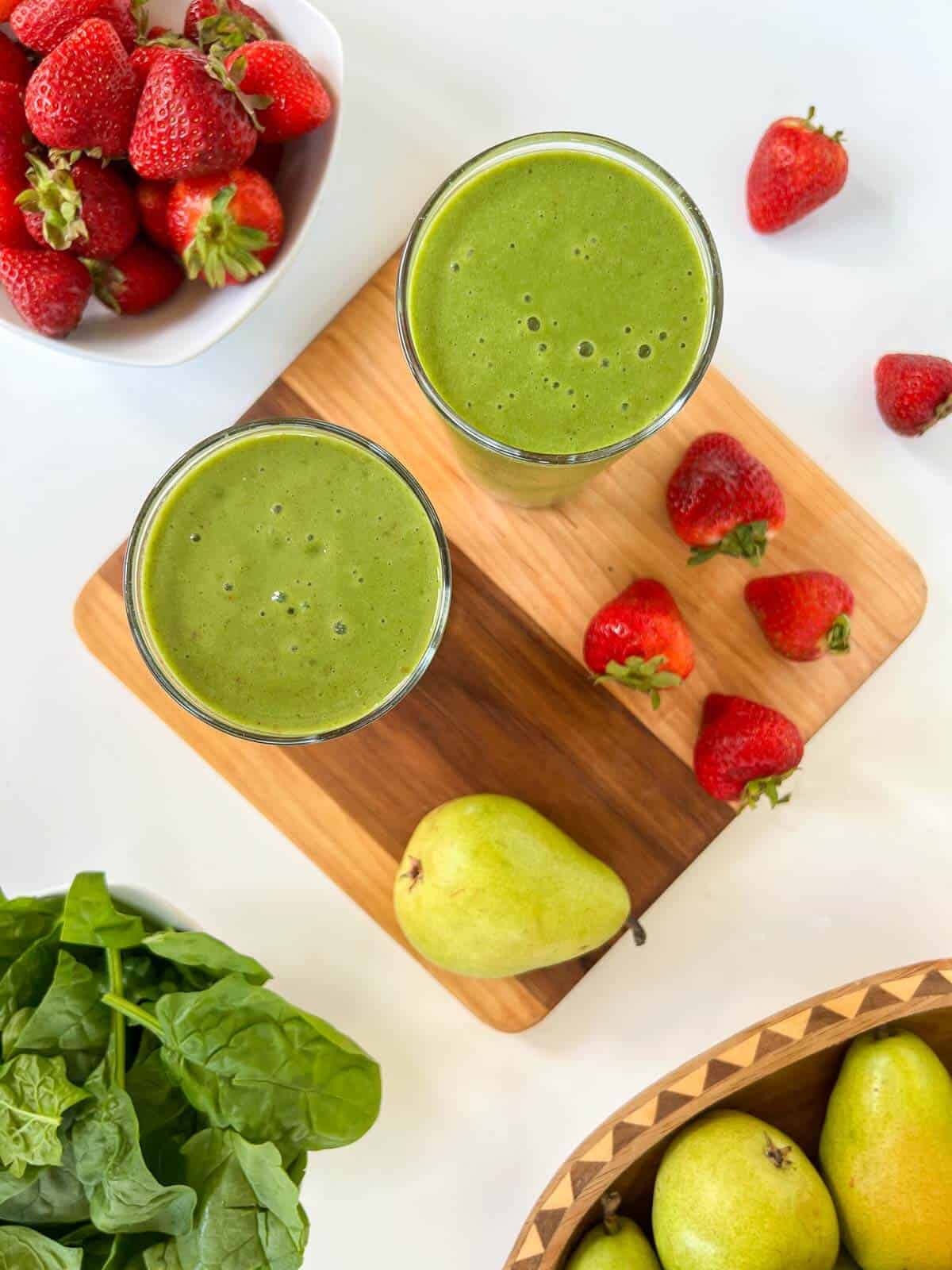 two glasses of spinach smoothie served with fresh produce on a table.