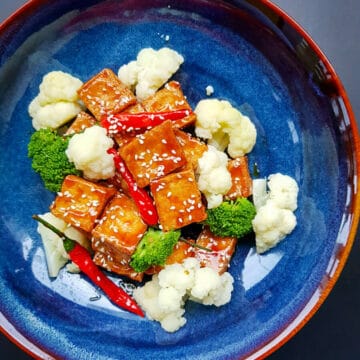 sesame tofu served in blue bowl with whole red chilies.