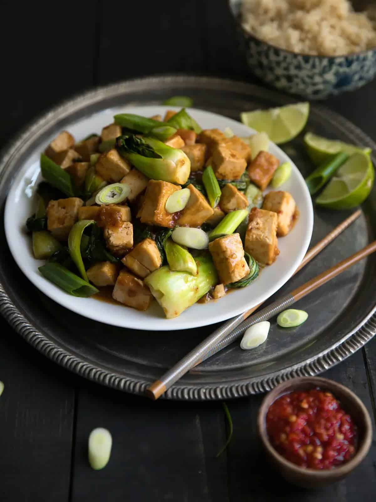 stir-fried tofu served with chili sauce on flat plates with chopsticks.