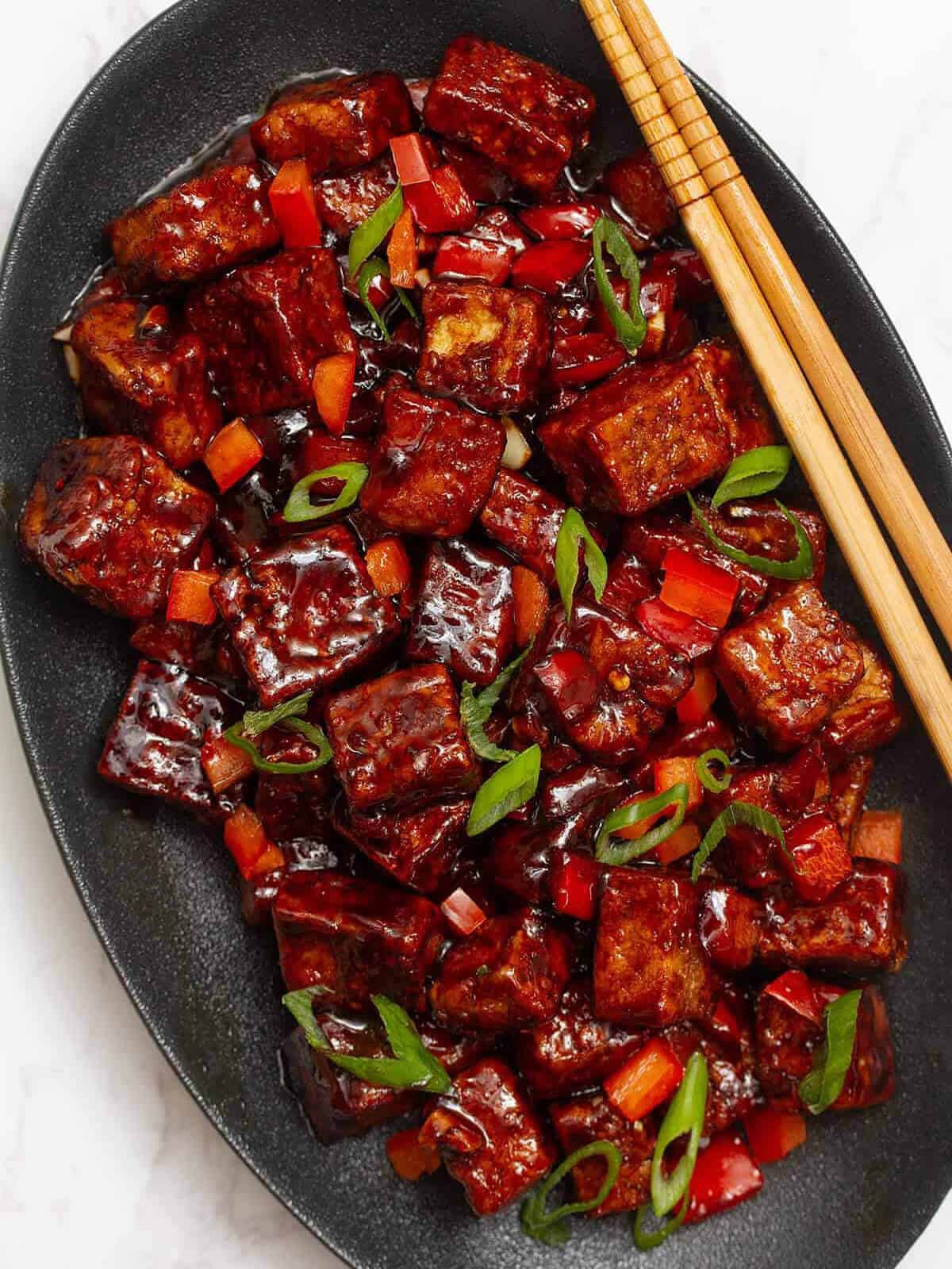 szechuan tofu served with chopstick on a dark serving plate.