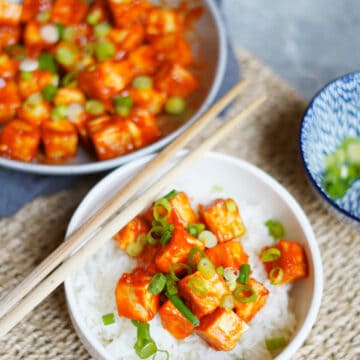 crispy gochujang tofu plate topped with green onions and served next to a pot.