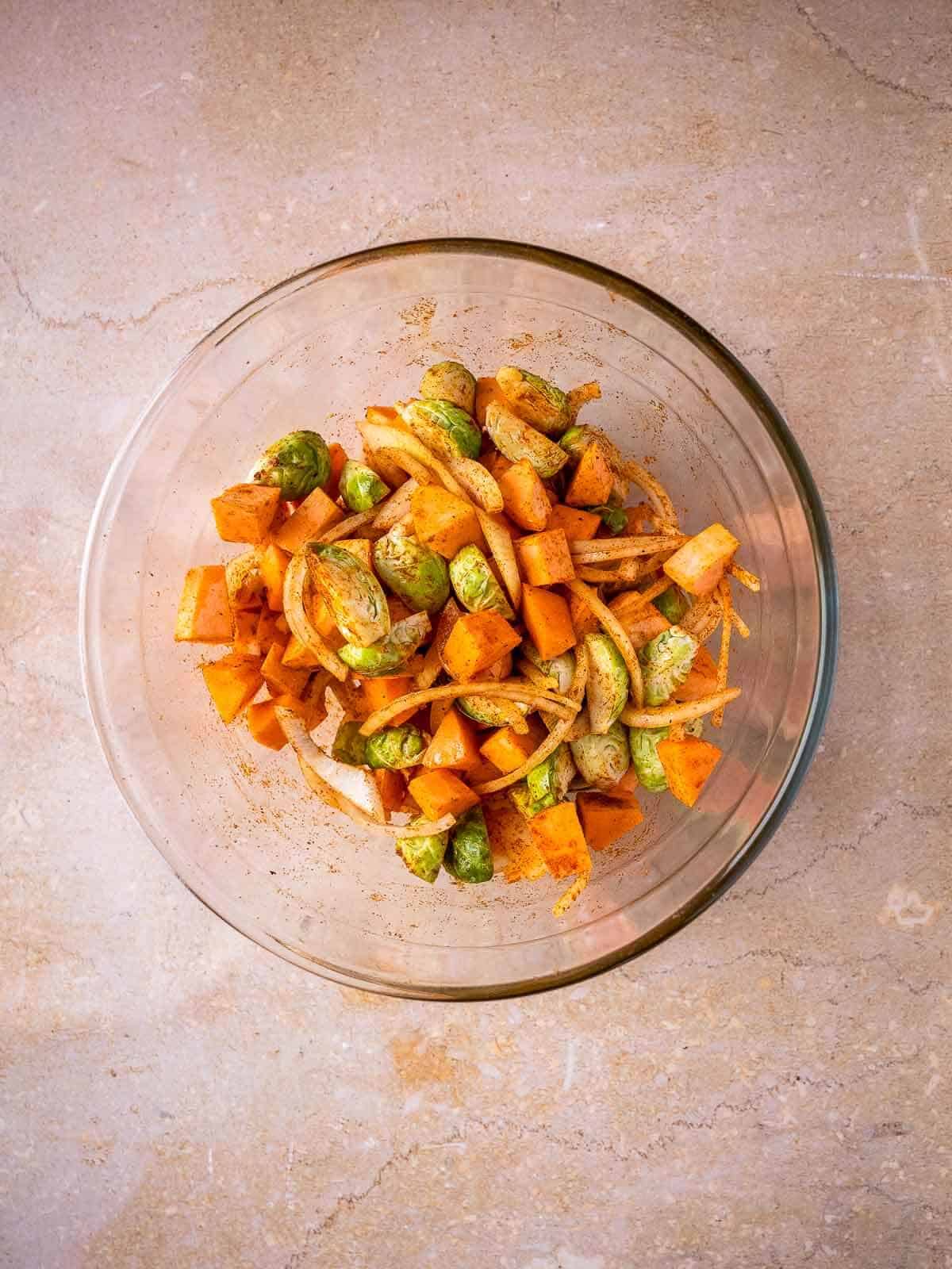 glass mixing bowl with vegetables and spices mixed.