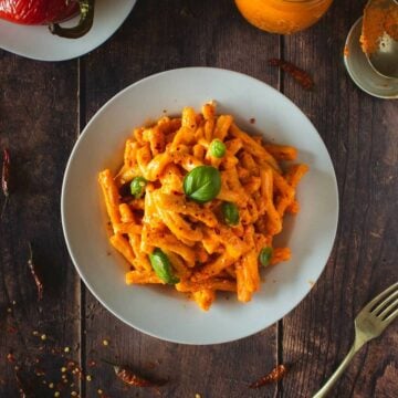 cooked pasta with tofu pesto served on a wooden table next to roasted peppers featured..