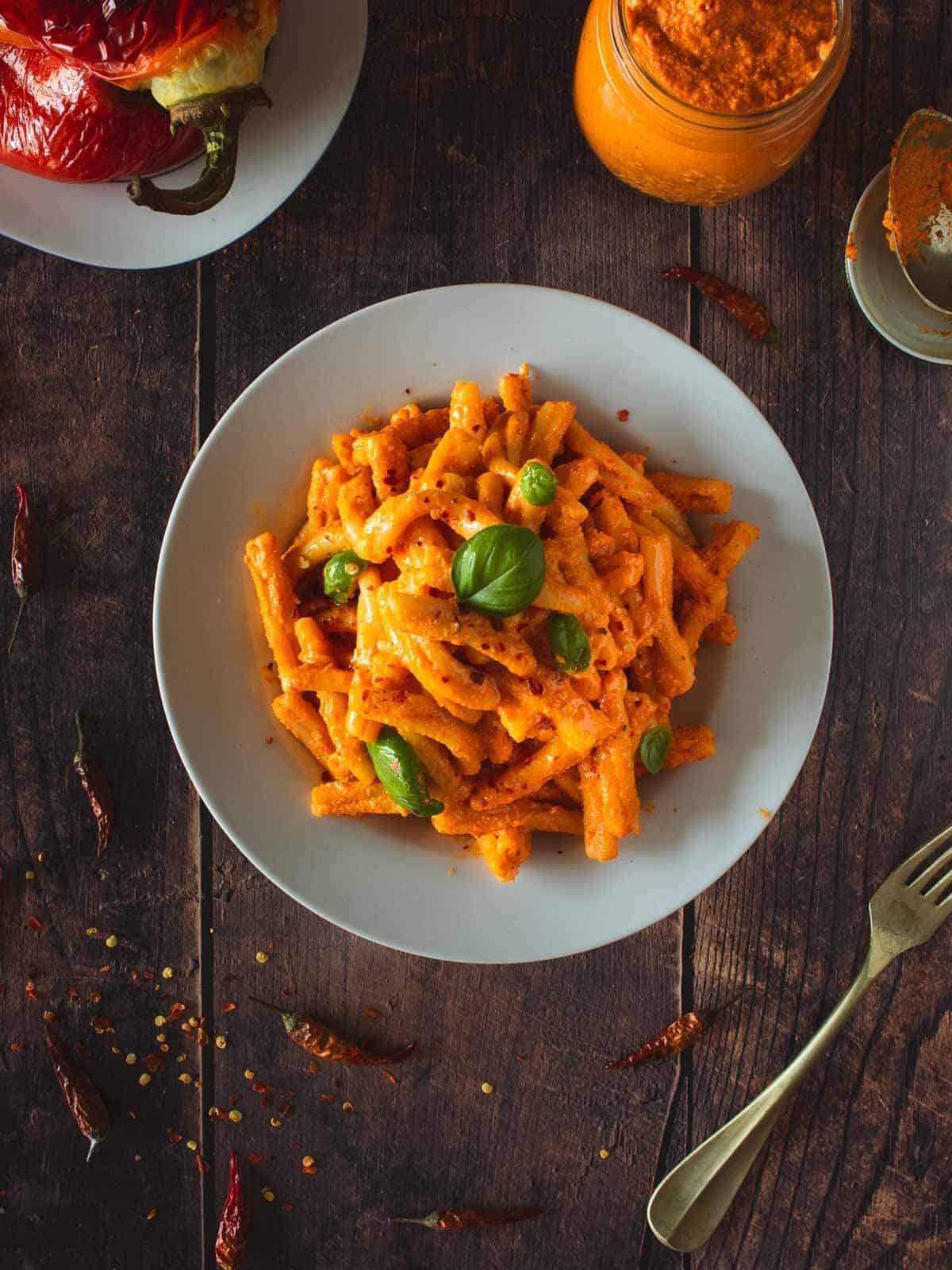 casarecce pasta with tofu pesto served on a wooden table next to roasted peppers.