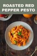 cooked pasta with tofu pesto served on a wooden table next to roasted peppers featured pin.