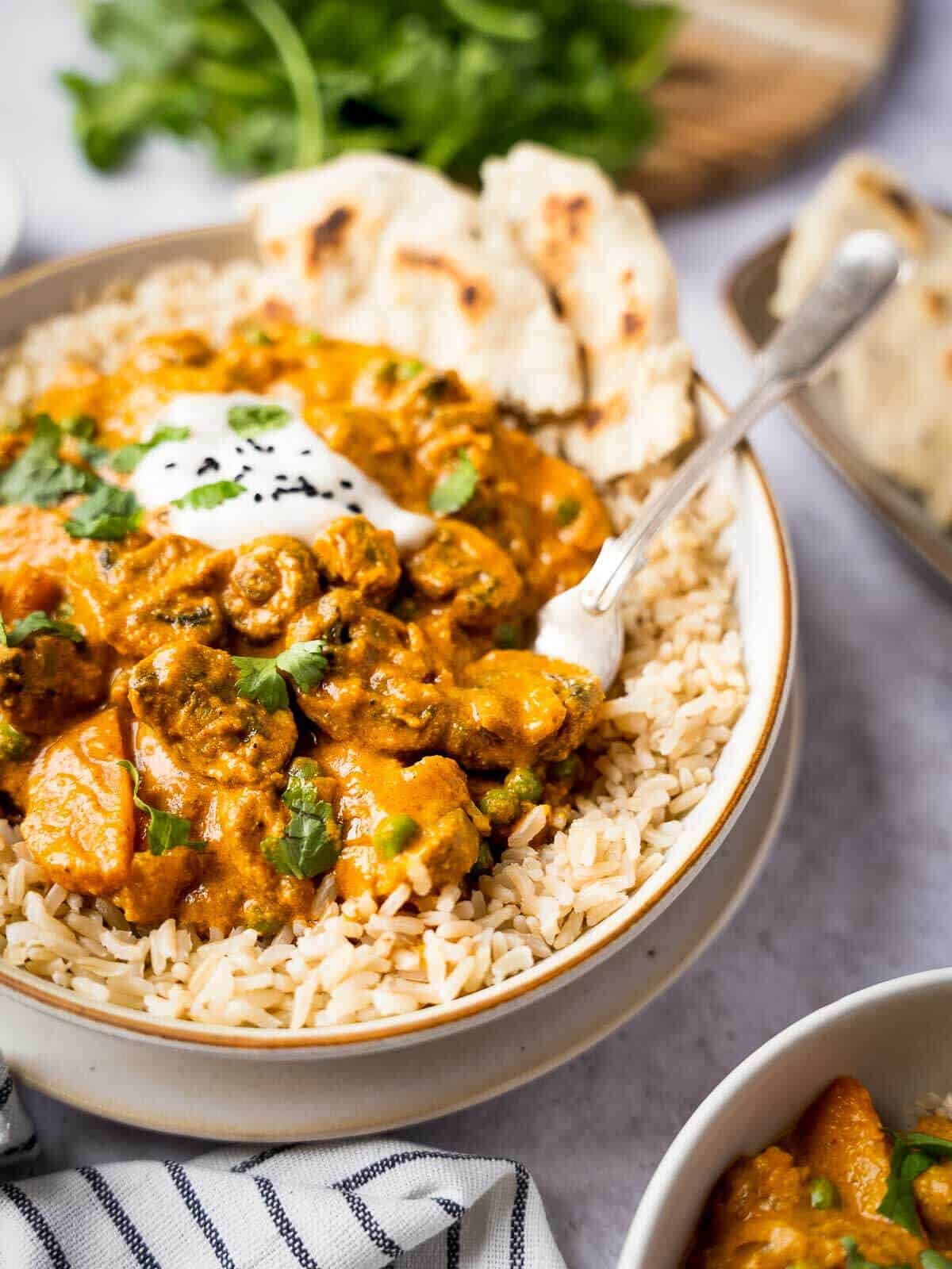 fork grabbing a bite of dairy-free tikka masala curry with a dollop of coconut yogurt, sesame seeds, and brown rice.