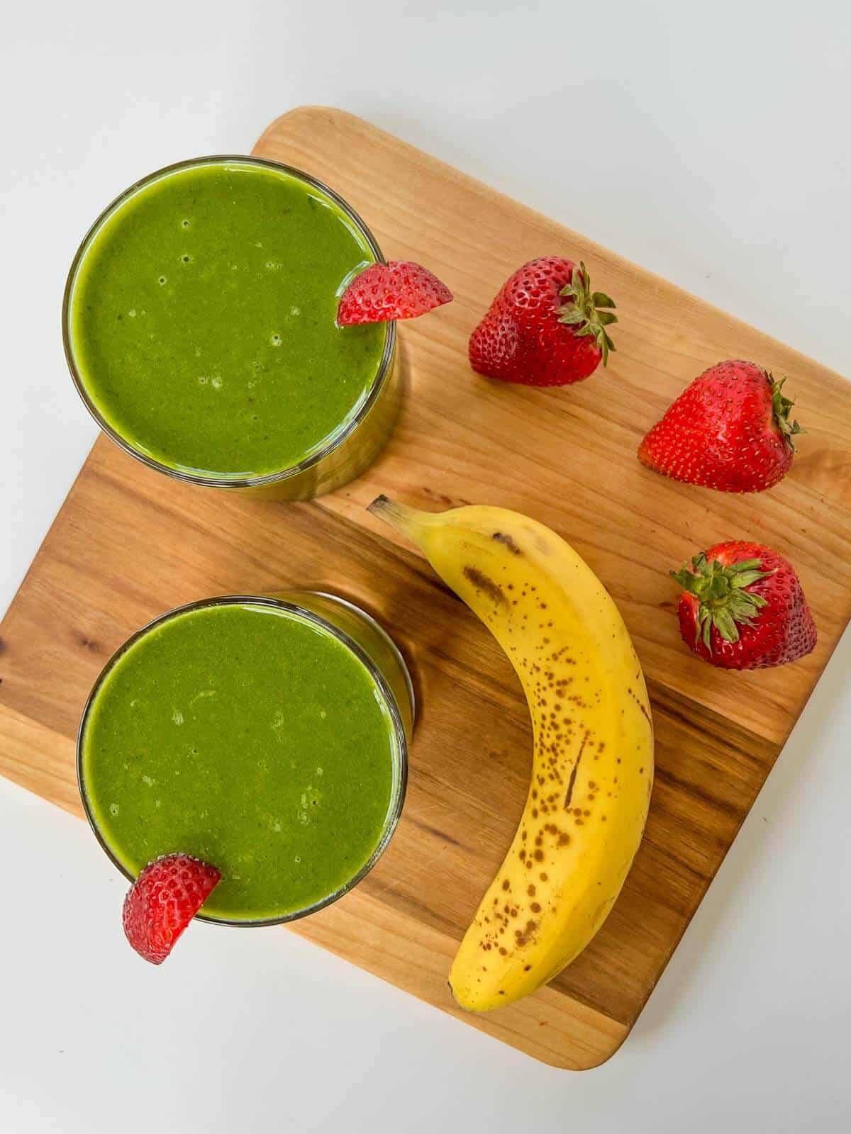 two smoothie glasses on a wooden table decorated with strawberries and bananas.