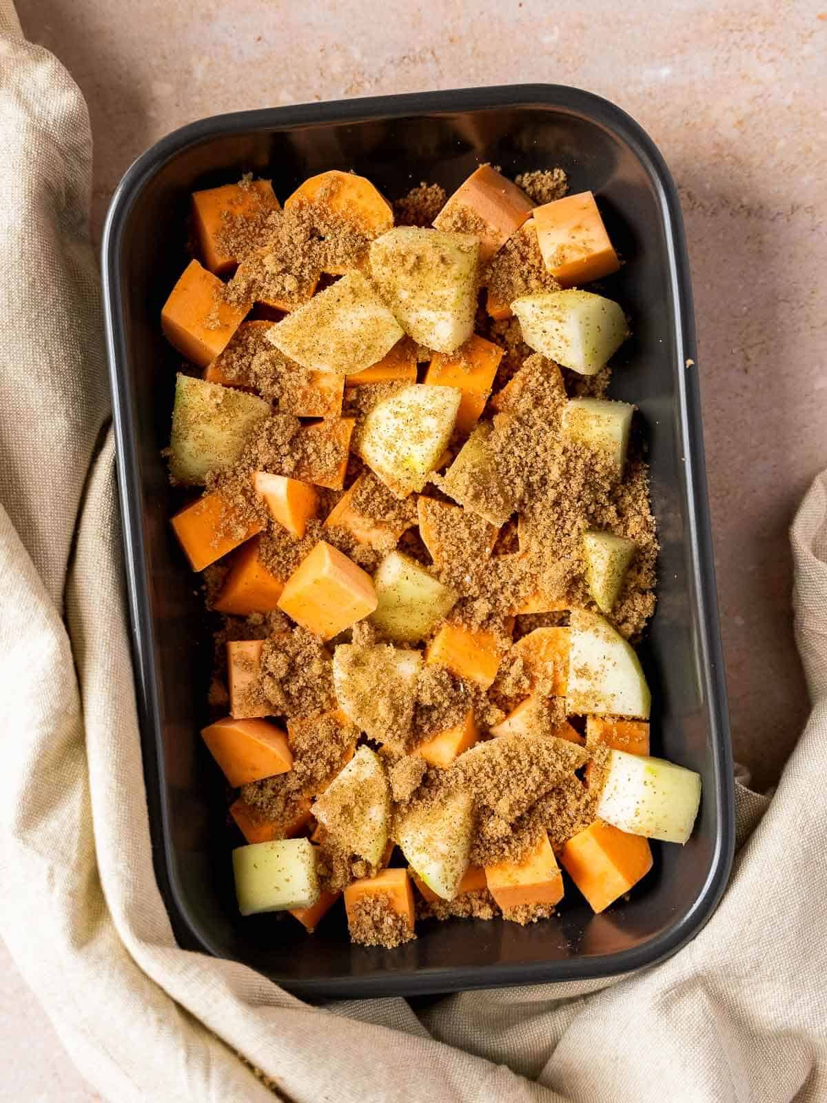 baking dish with sweet potato and apple dice covered with brown sugar and spices mixture.