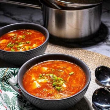 Tomato, enoki, and tofu Chinese soup in a bowl next to a pot.