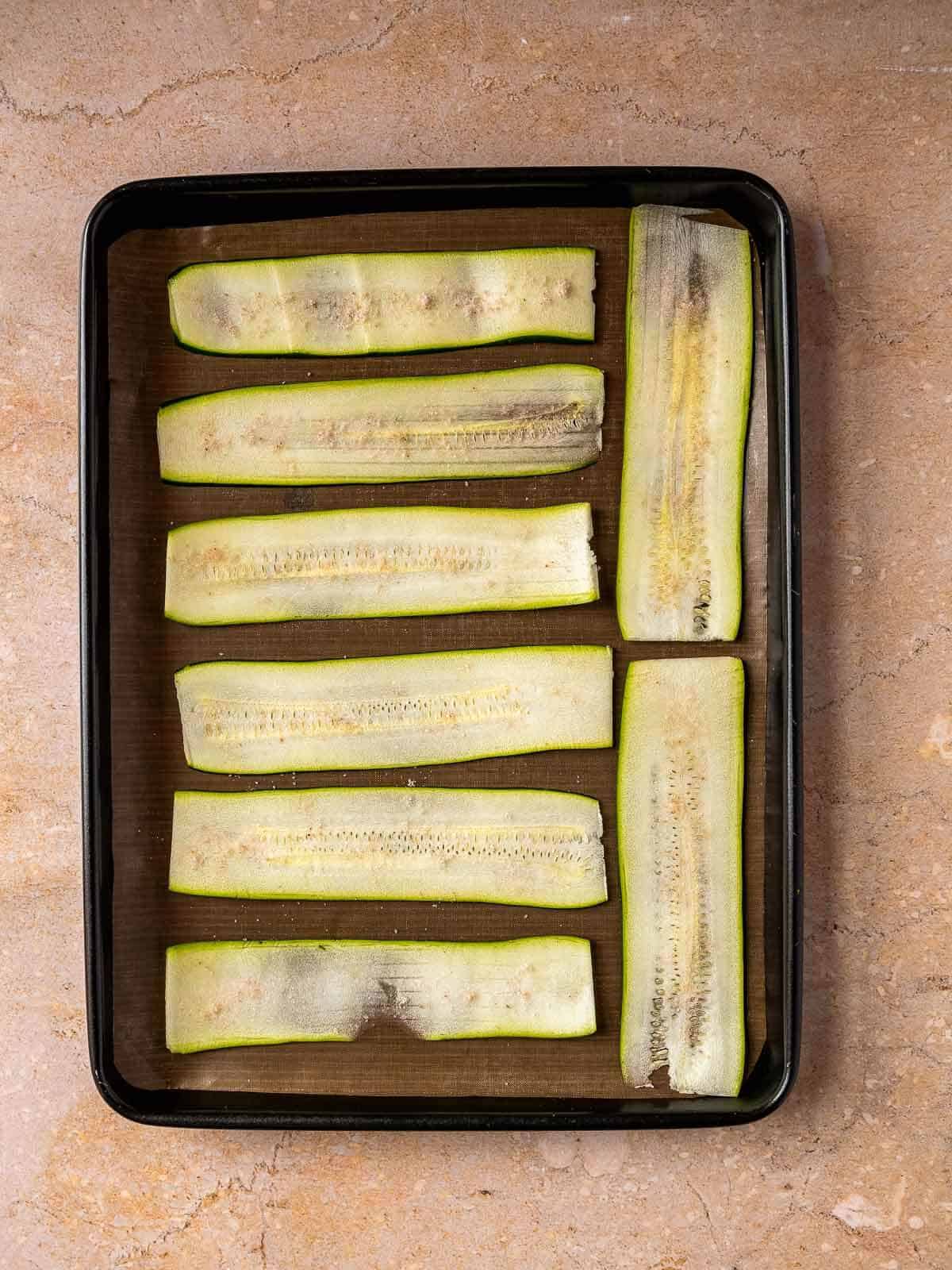 sprinkle salt on top of the zucchini slices laying on a baking dish.