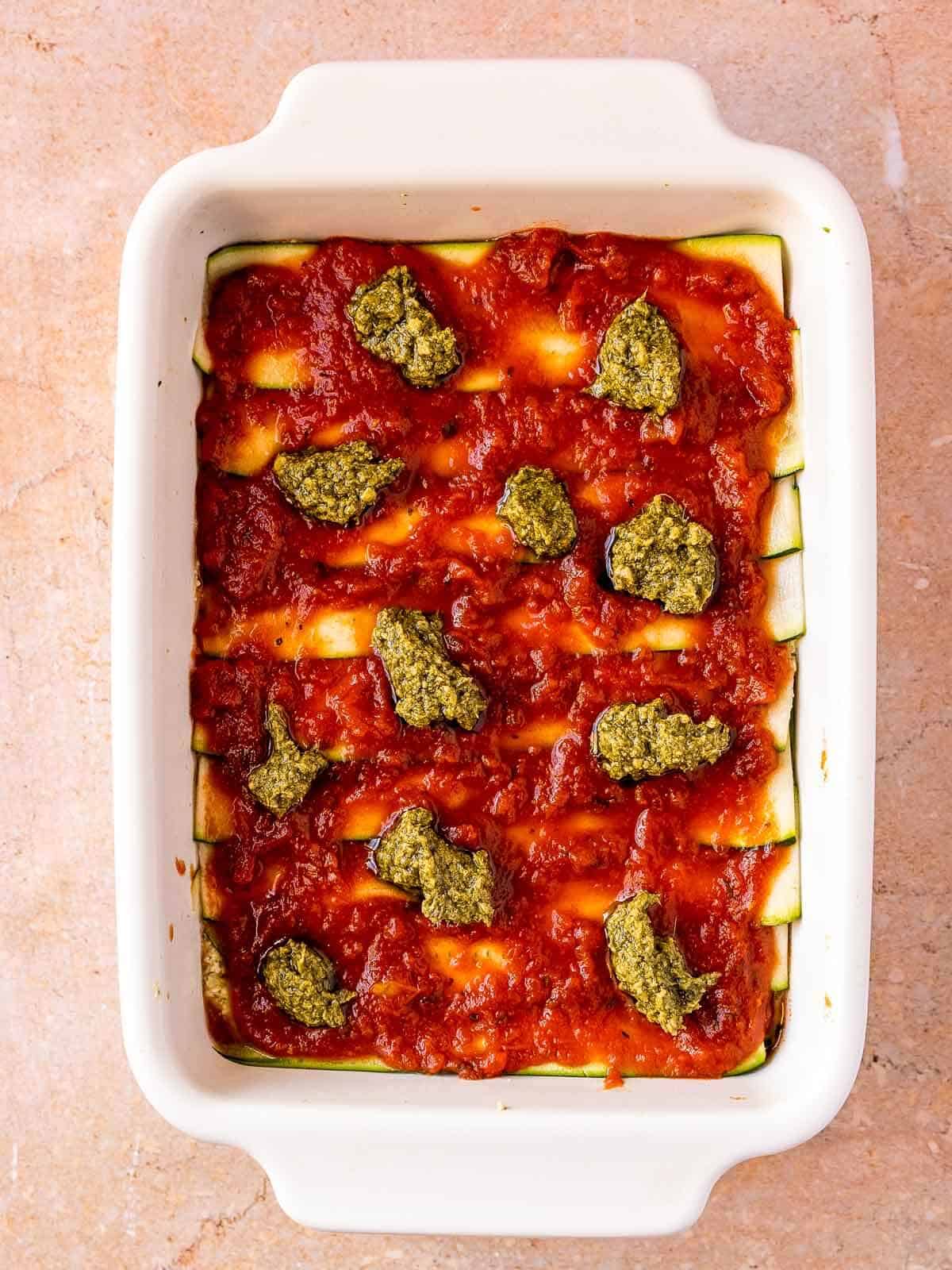uncooked vegan zucchini casserole with vegan pesto dollops on top.