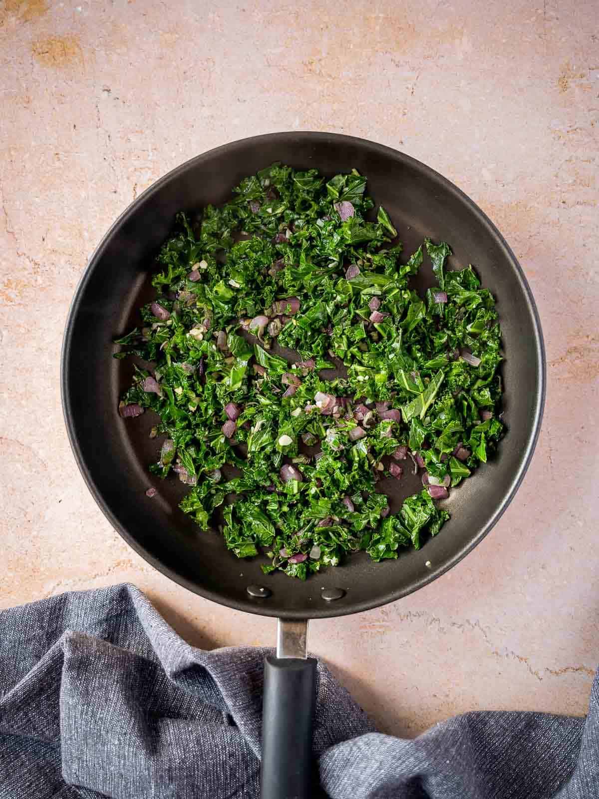 stir frying the chopped red onions with kale and herbs.