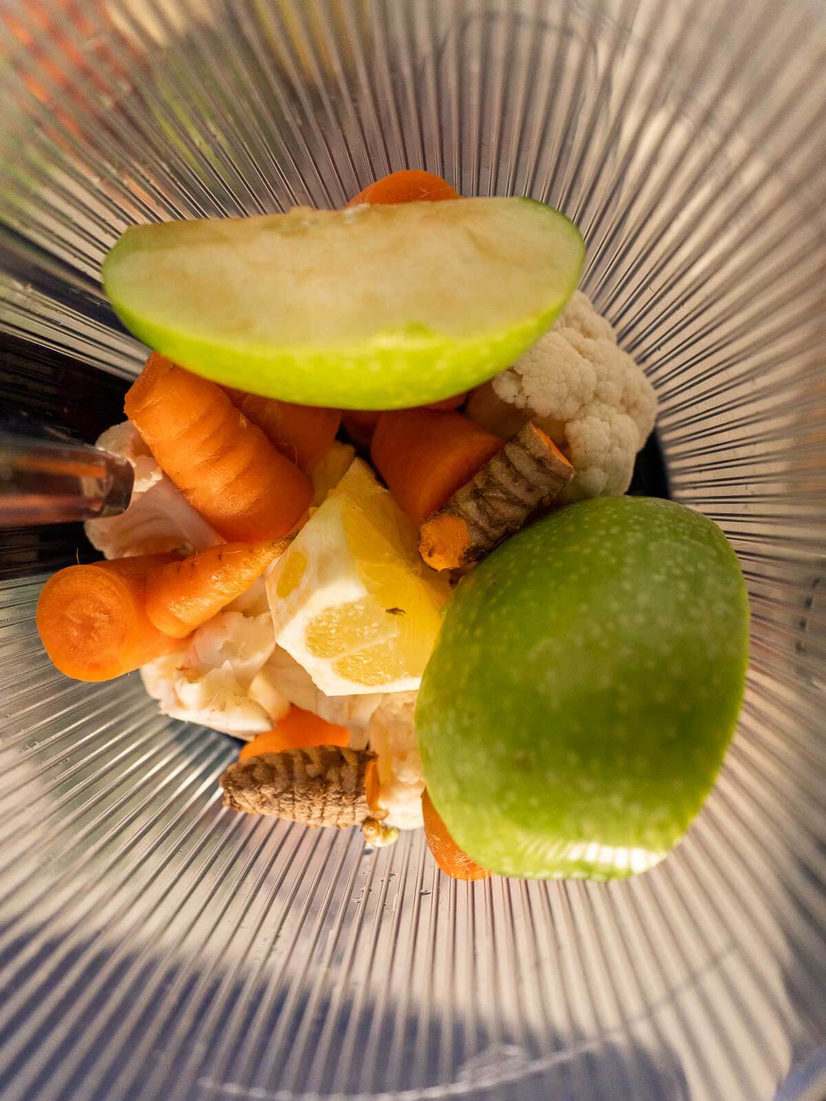 fresh chunks of carrot,, ginger, turmeric, lemon and cauliflower in juicer jar.