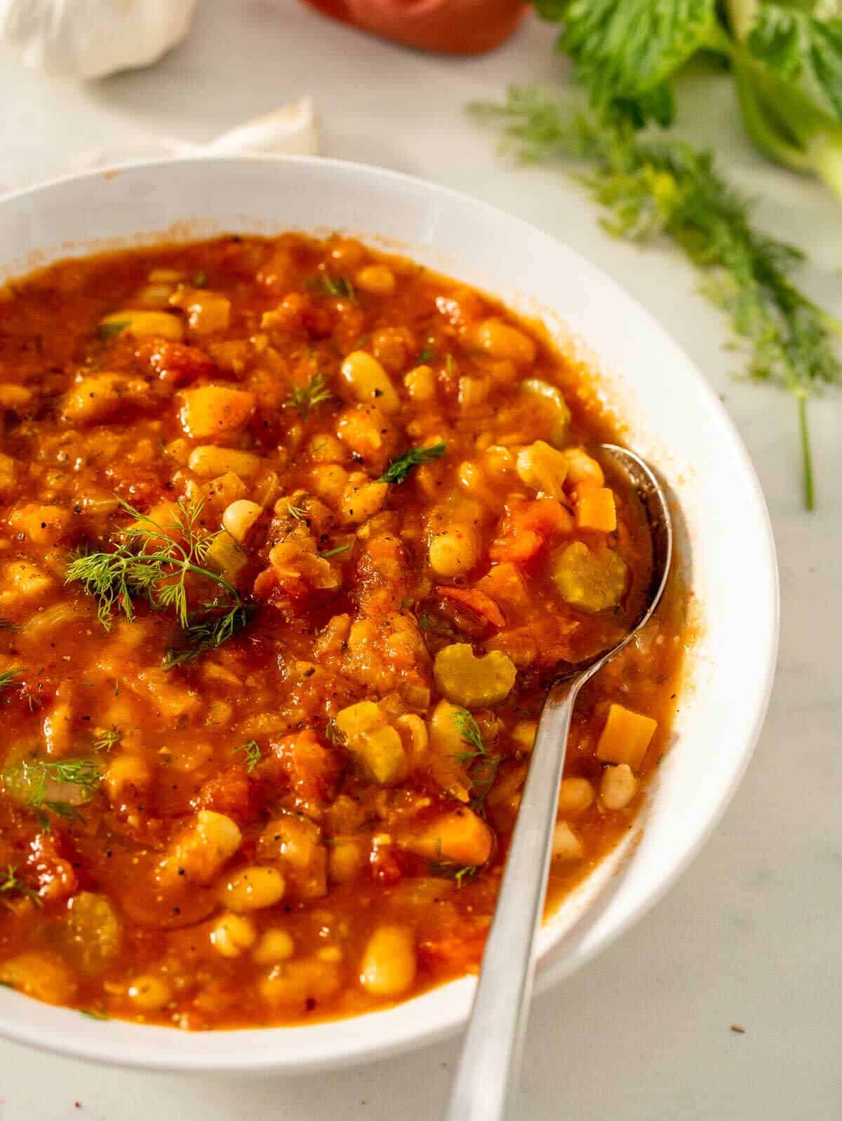 spoon on a plate with fasolada greek white bean soup.