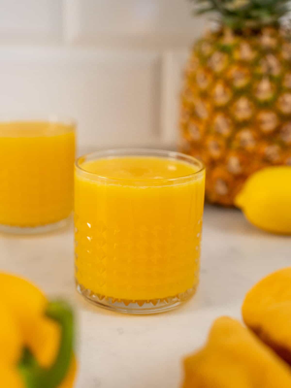 Golden Pineapple and Ginger juice glasses served with fruit on the background.