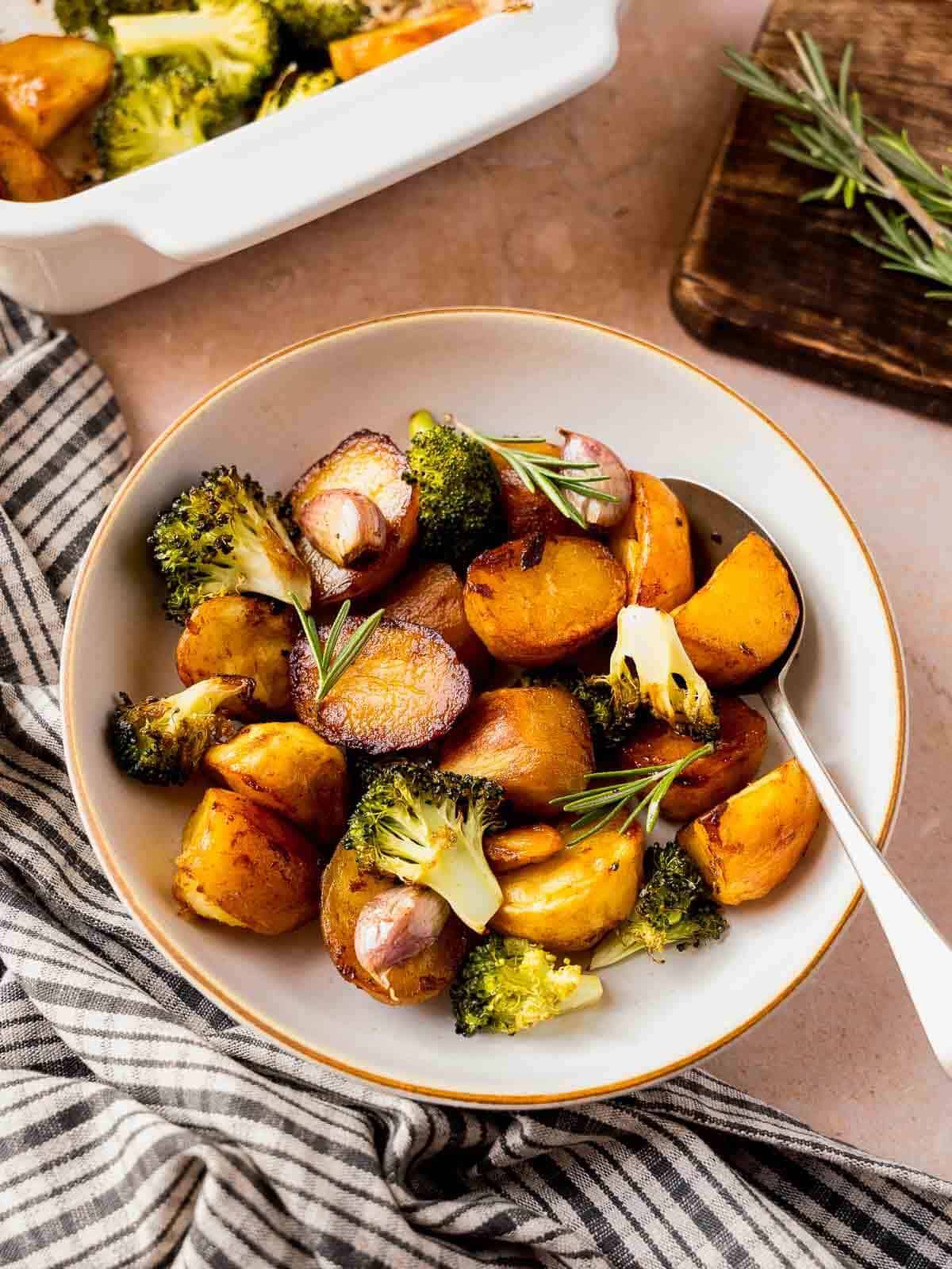 vegan roasted garlic and rosemary potatoes with marmite next to casserole dish and table with herbs.