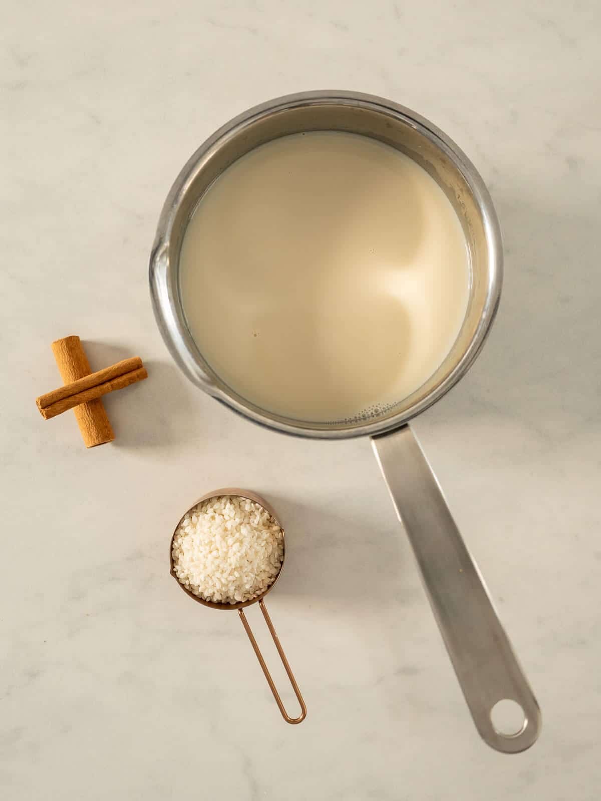 ingredients to make vegan rice pudding on a table, oat milk, cinnamon, and rice.