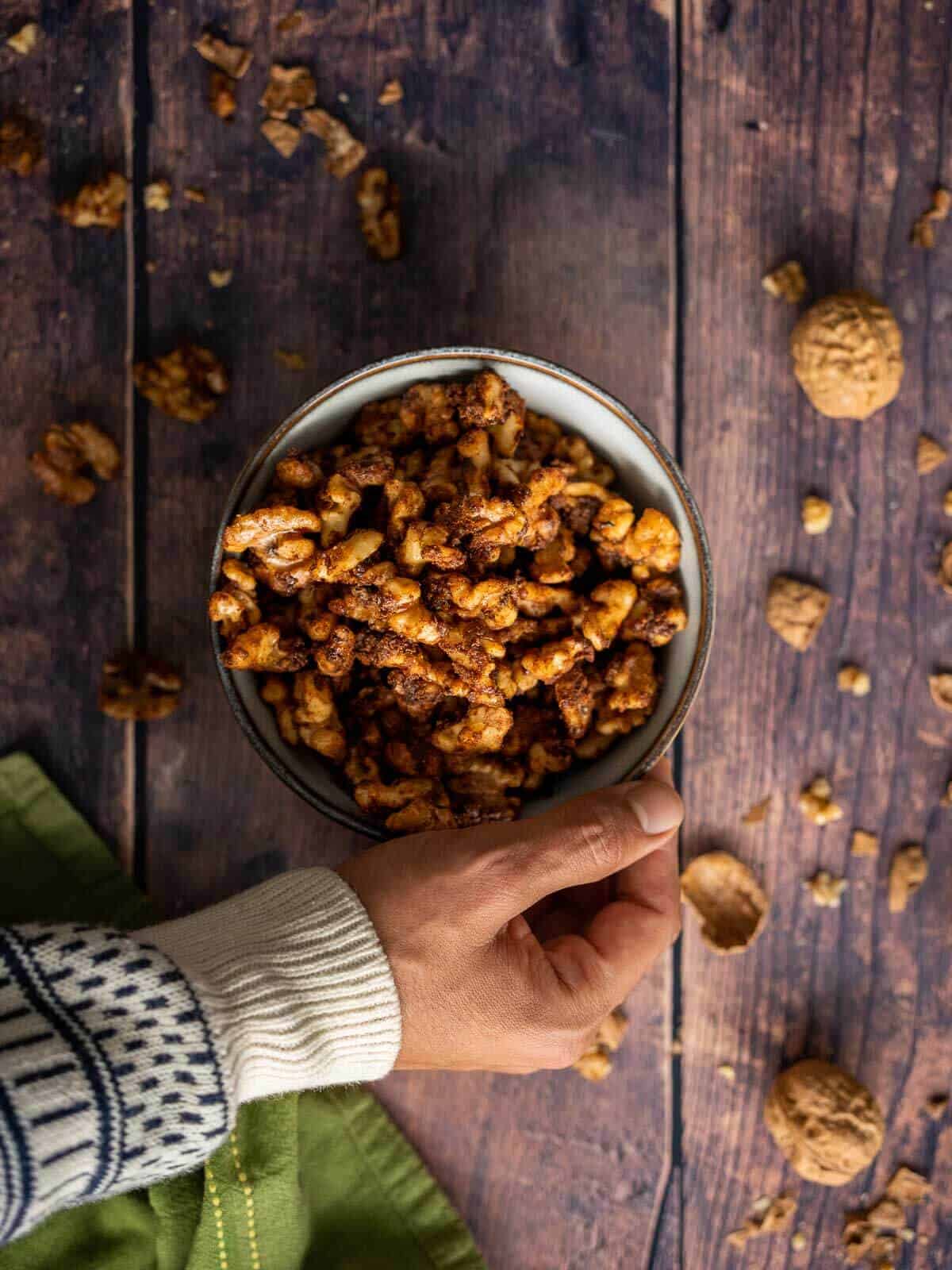 hand holding bowl with brown sugar candied walnuts.