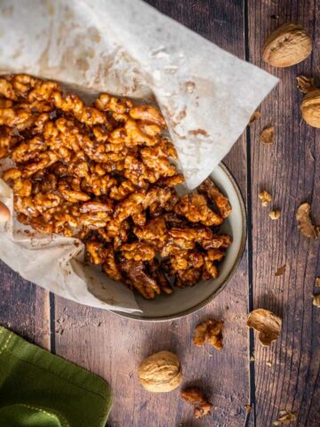 pouring candied walnuts from parchment paper to a bowl.