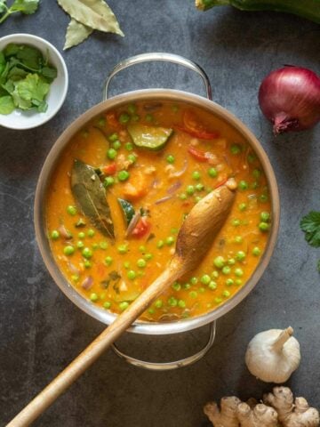 pot with coconut chickpea curry with a wooden spoon.