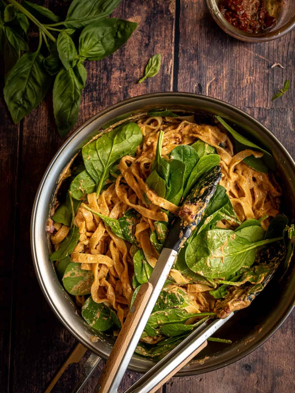 Folding Spinach fettuccine pasta in a skillet.