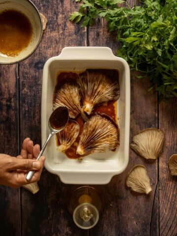adding marinade on top of the blue oyster mushrooms in a casserole dish.