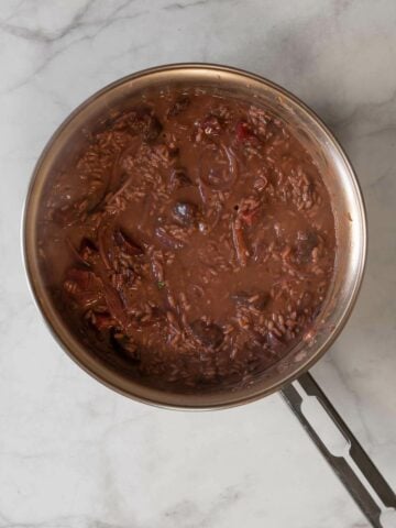 adding vegetable broth into the red risotto saucepan.