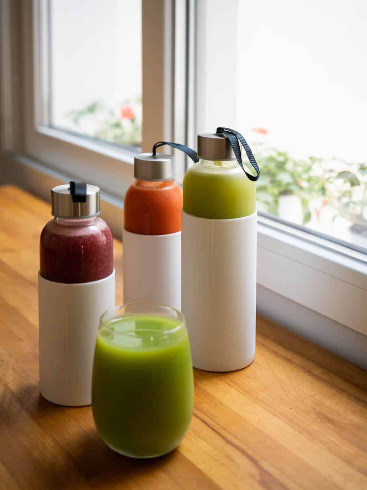 storing juice tips, three airtight glass containers with white silicon sheath and glass of celery juice.