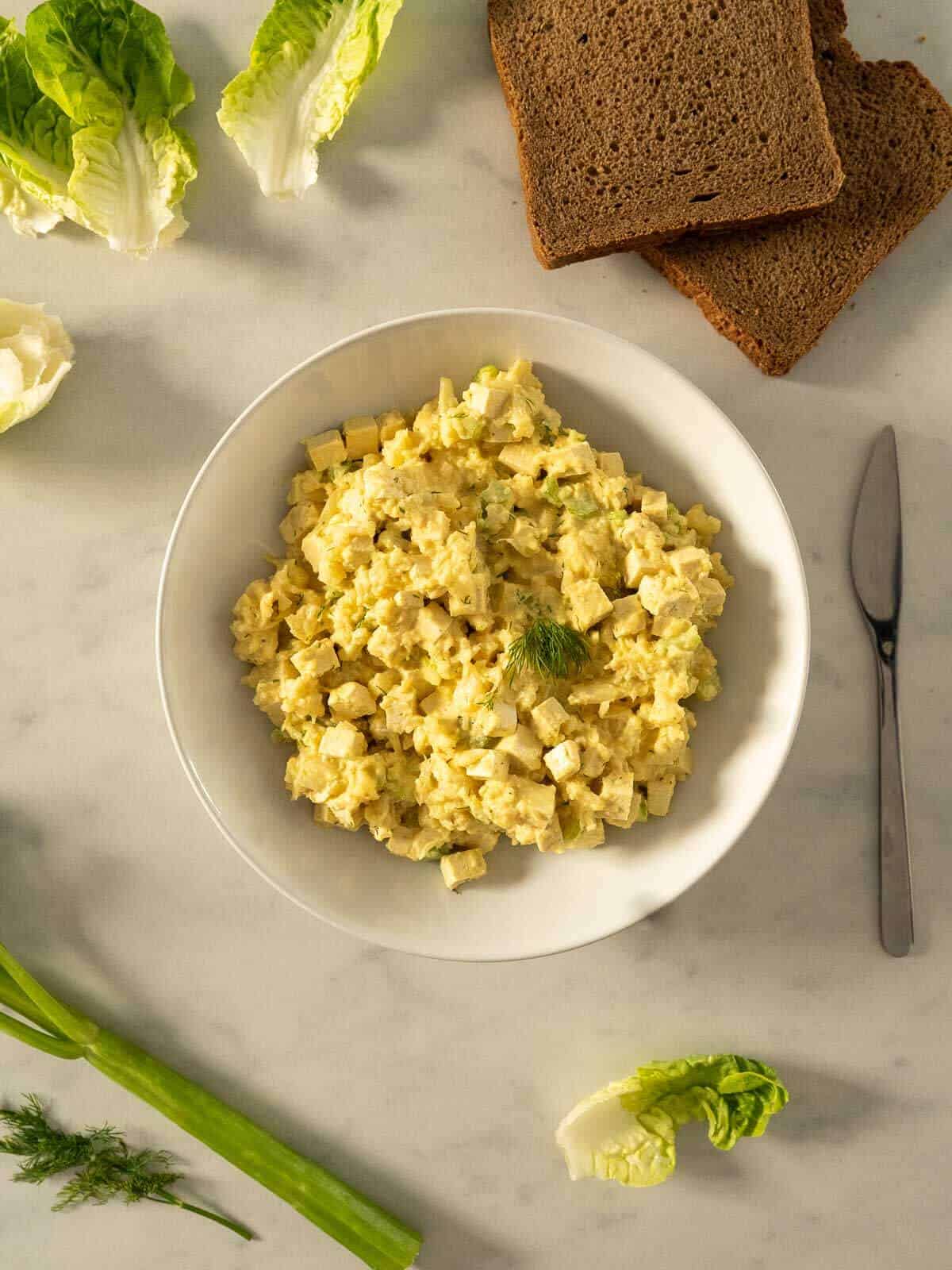 egg salad bowl served next to lettuce leaves and rye bread slices.