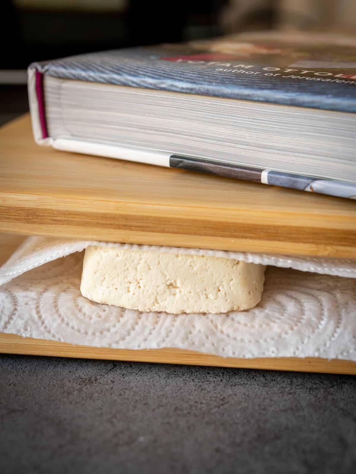 press tofu slices between paper towels and place heavy objects like books on tops.
