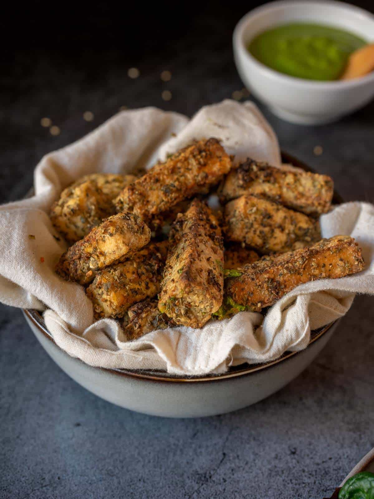 crispy air fryer tofu nuggets with mediterranean marinade and green creamy sauce behind.