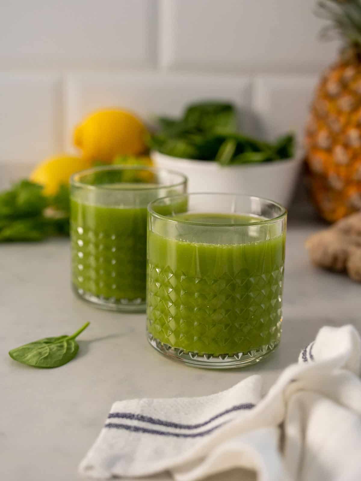 two glasses of pineapple ginger juice with spinach and cucumber.