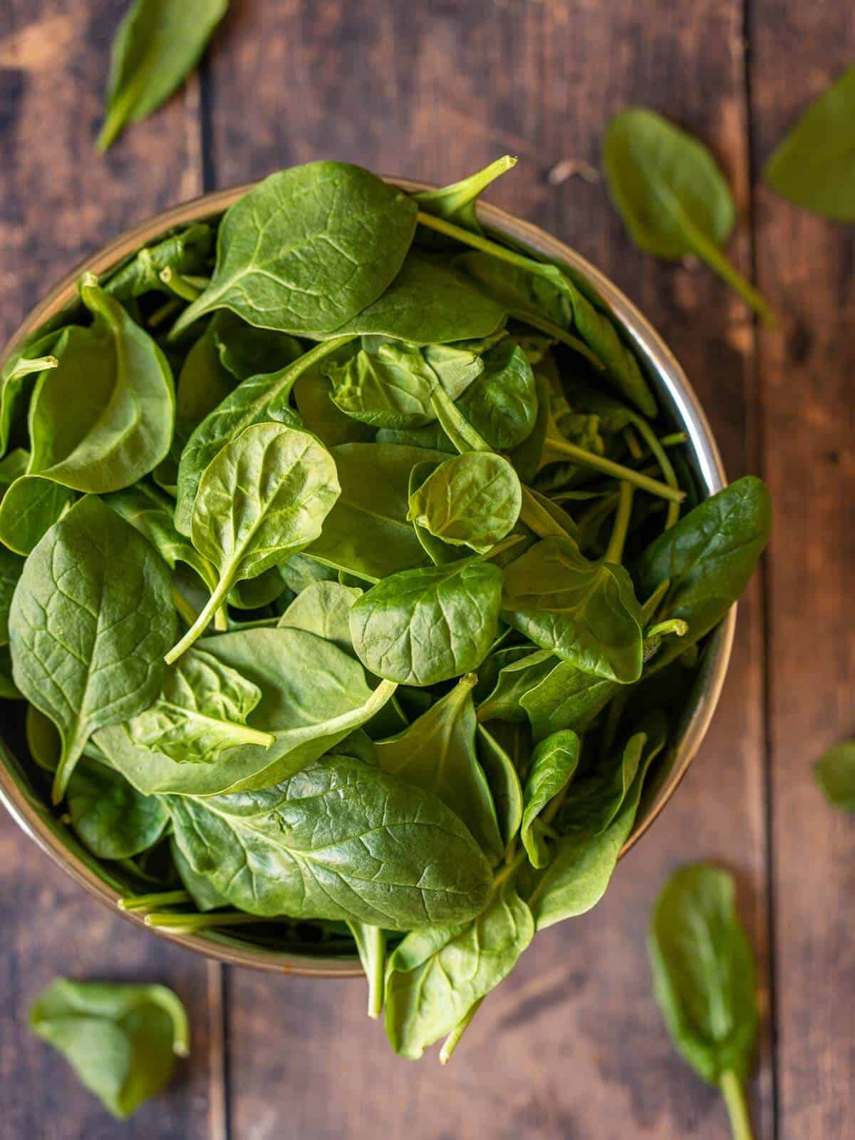 bowl of fresh baby spinach on wooden table.