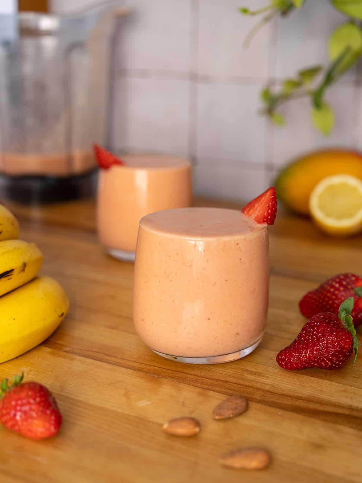 two glasses of strawberry banana mango smoothie served with a blender behind.