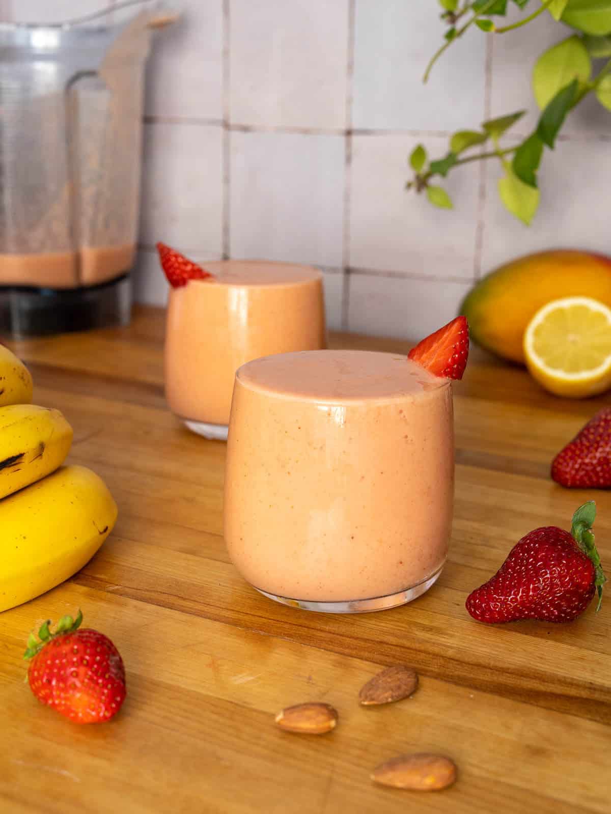 two glasses of strawberry mango banana smoothie served with a blender behind.