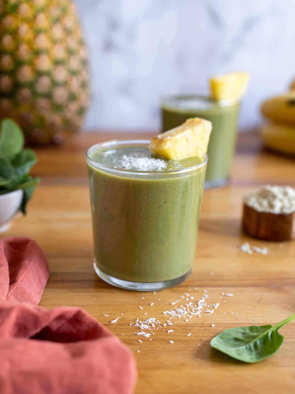 two pineapple banana spinach smoothies on a wooden table.