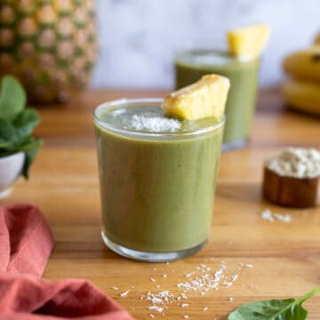 two pineapple banana spinach smoothies on a wooden table featured.
