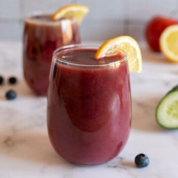 glass of organic blueberry juice garnished with a lemon wedge.