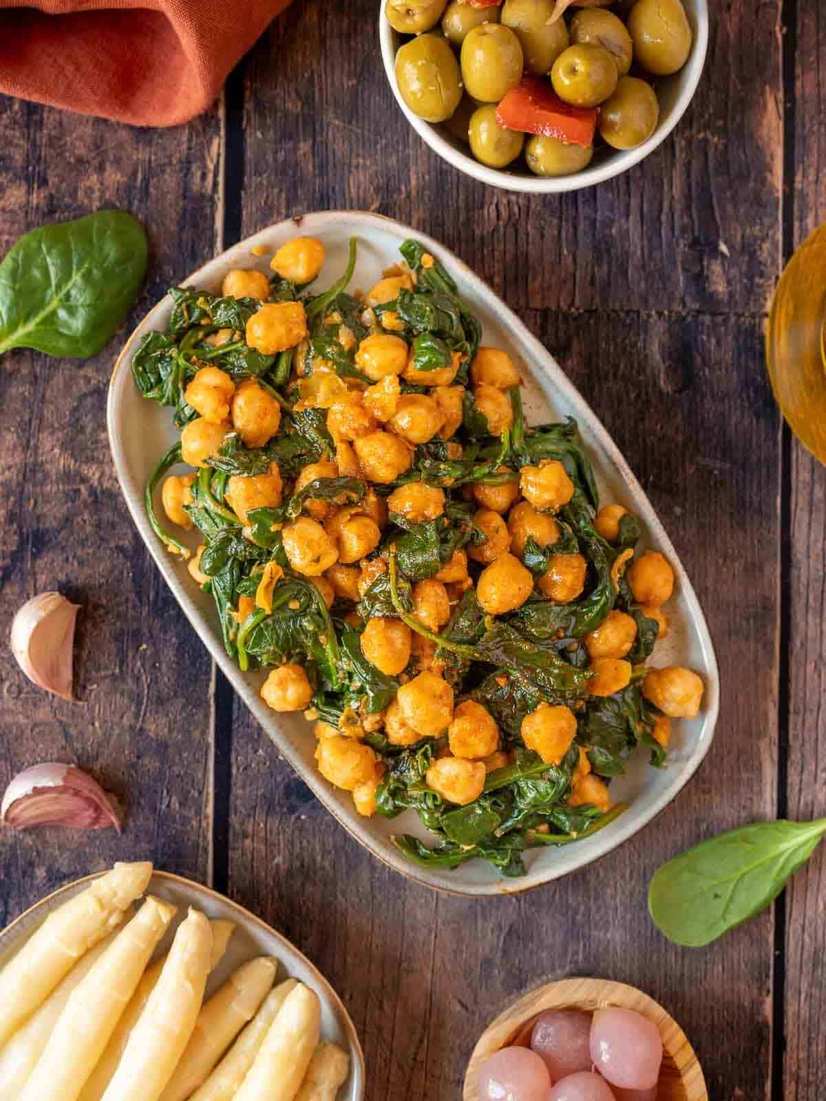 spanish sauteed chickpeas with spinach on a classic Spanish table with asparagus, olives, and pickled onions.