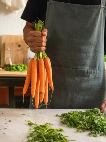 man holding a bunch of carrots, tops removed.