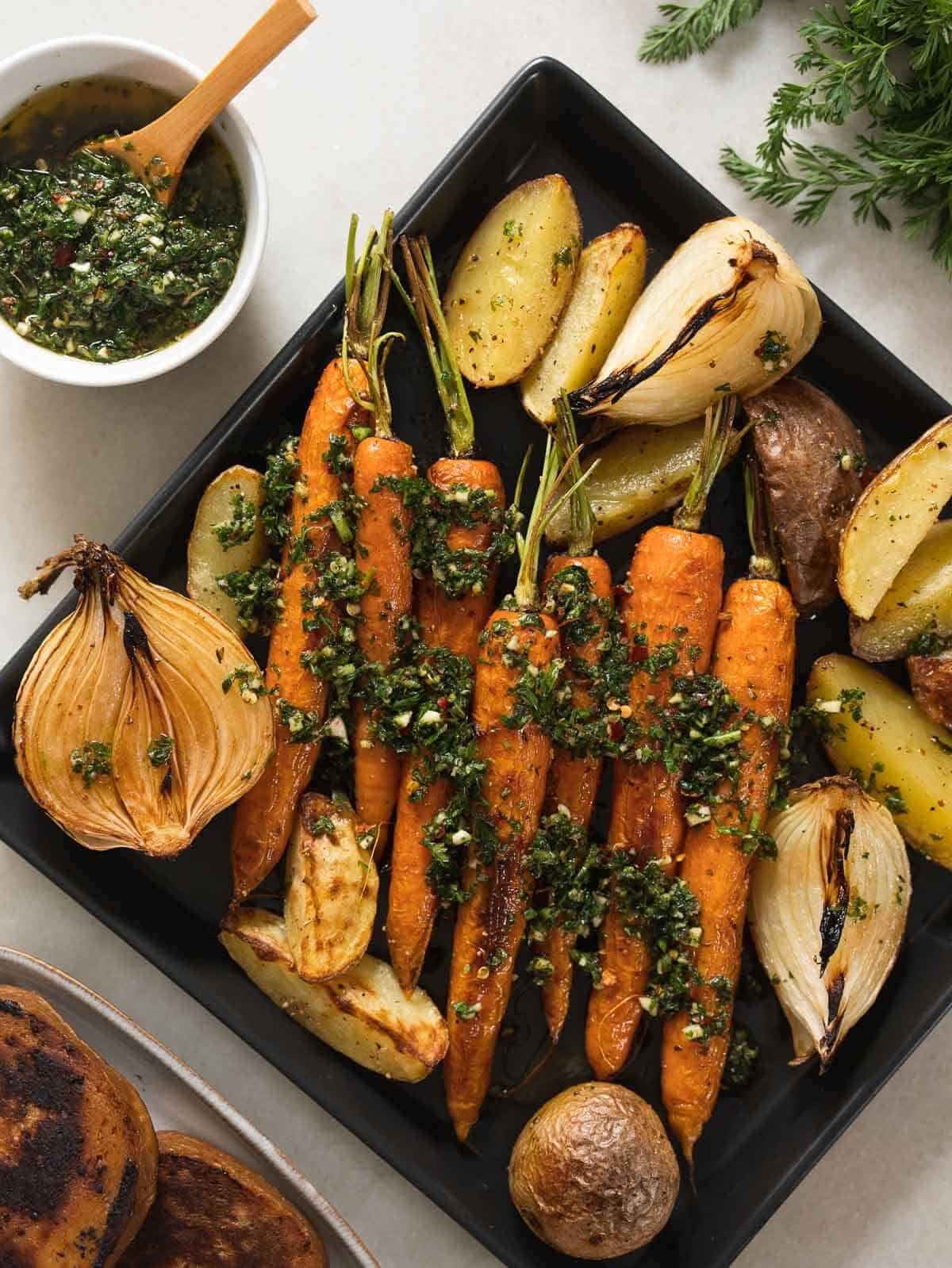 square plate with roasted vegetables drizzled with carrot tops chimichurri.