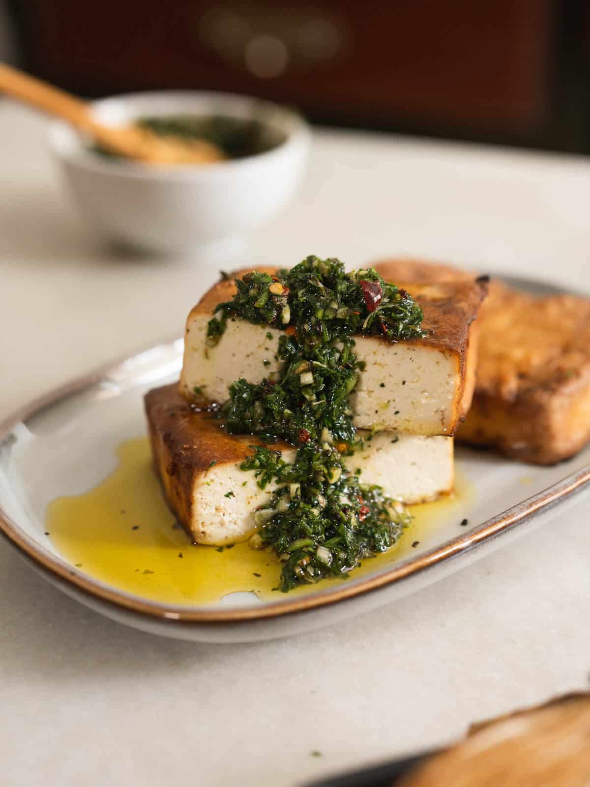 pan-fried tofu steaks topped with carrot tops chimichurri.