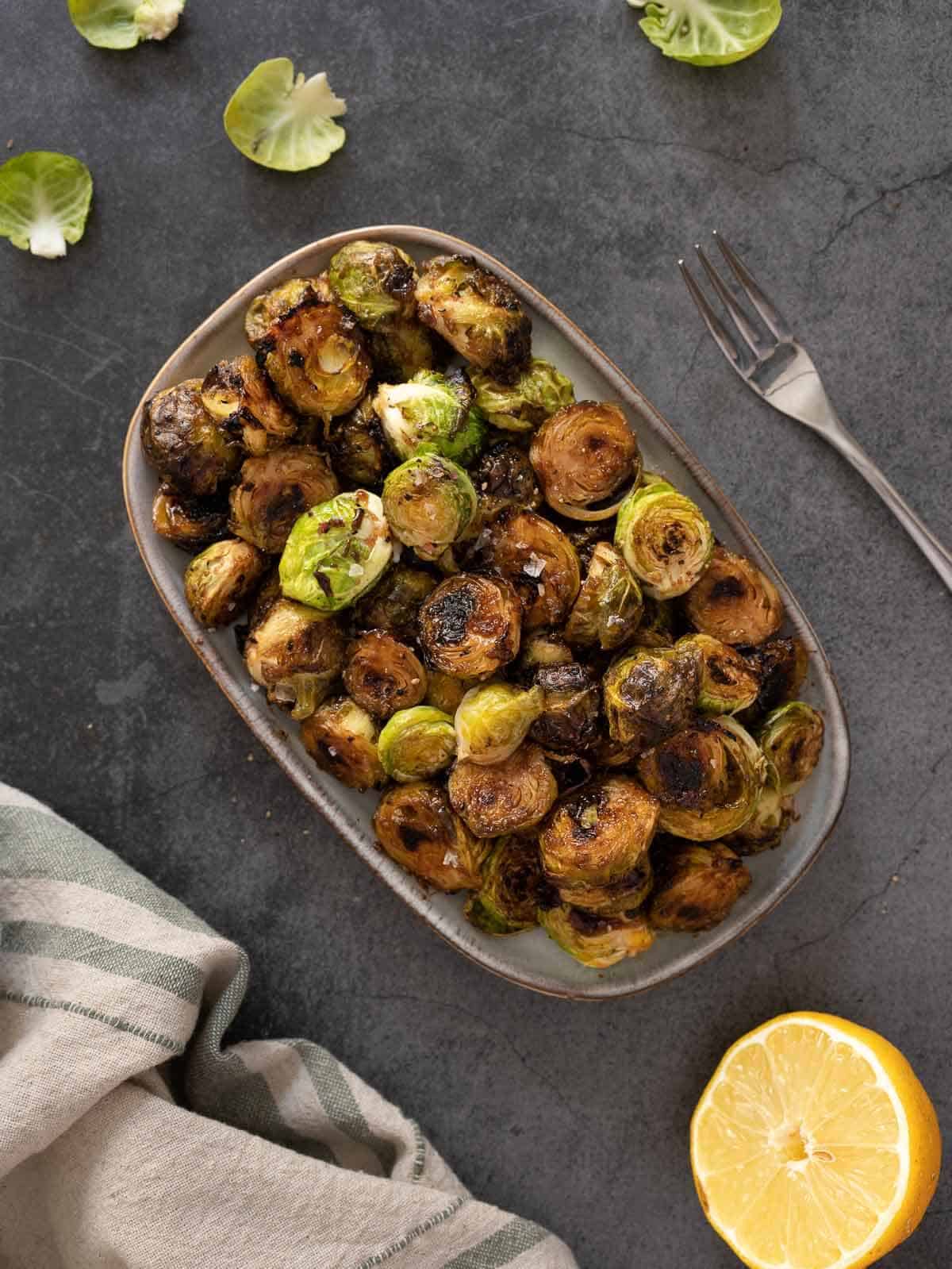 roasted balsamic lemon marinated Brussels sprouts plated with half a lemon by its side.