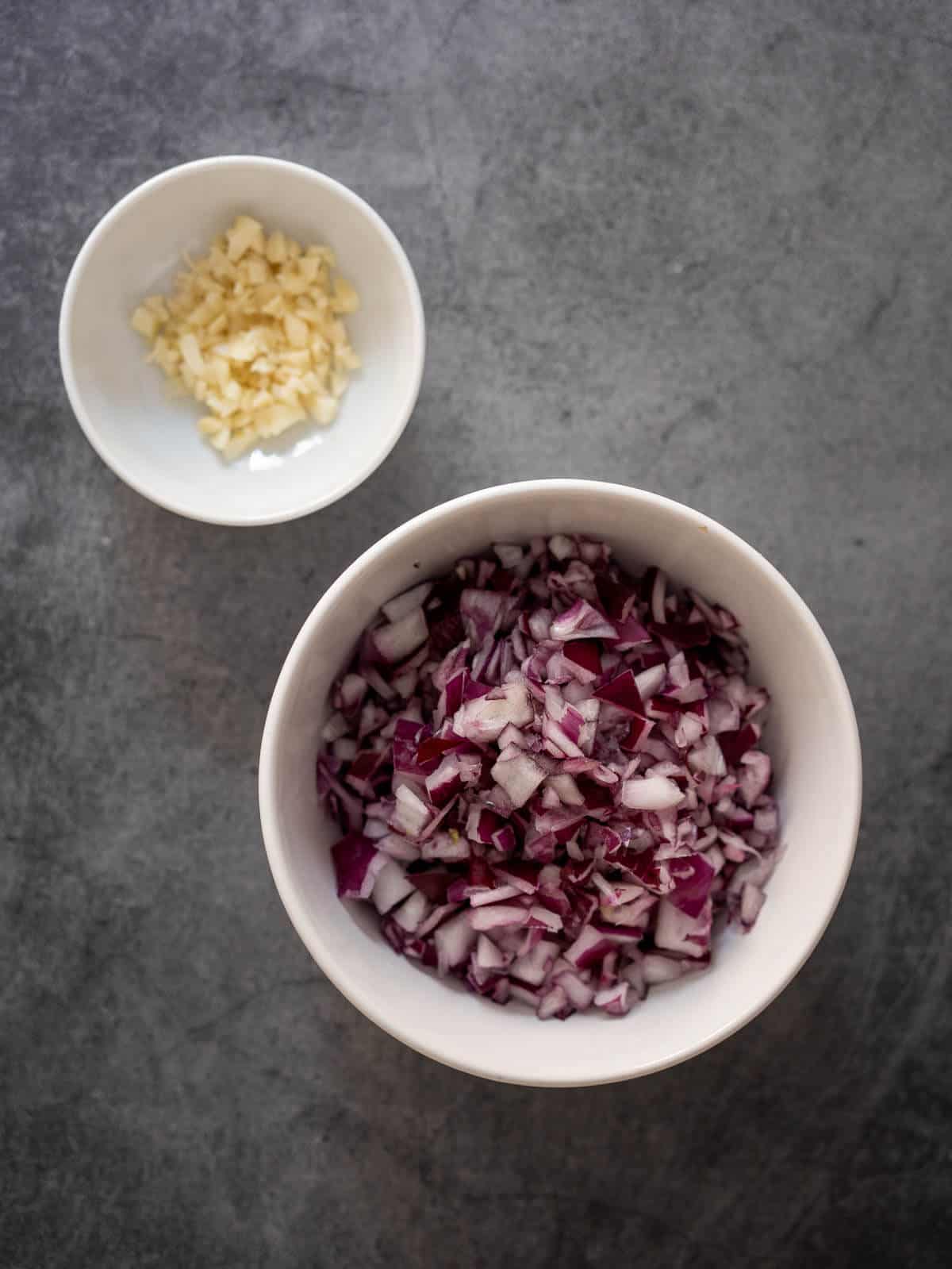 two bowls with chopped garlic and red onions.