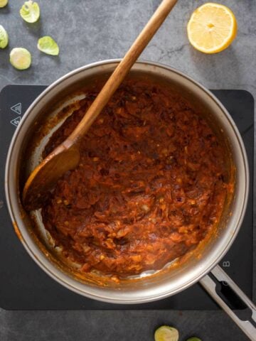 cooking tomato sauce with garlic, onions, and spices until the sauce thickens.