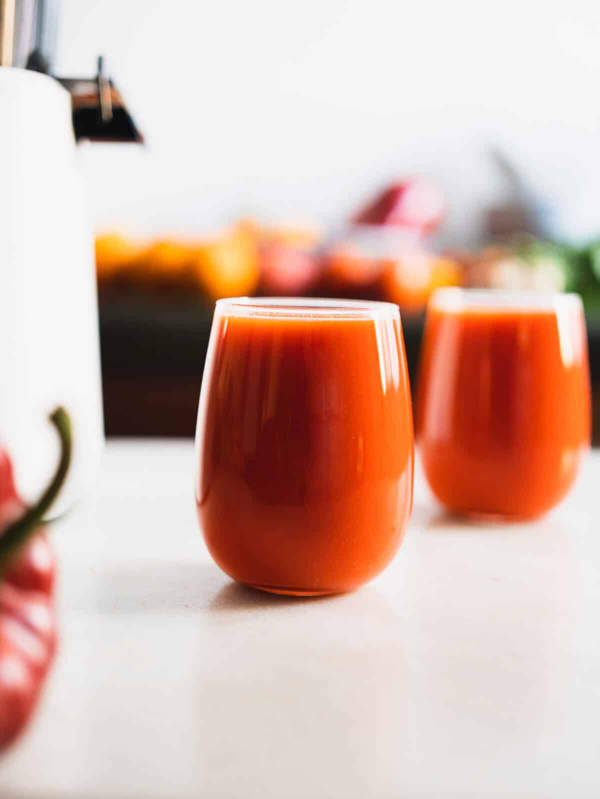 two glasses of red juice next to the juicer.