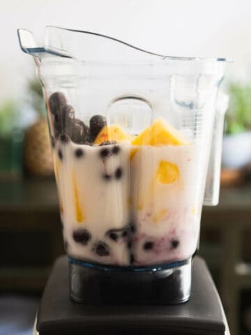 blender jar with coconut milk, blueberries and pineapple chunks.