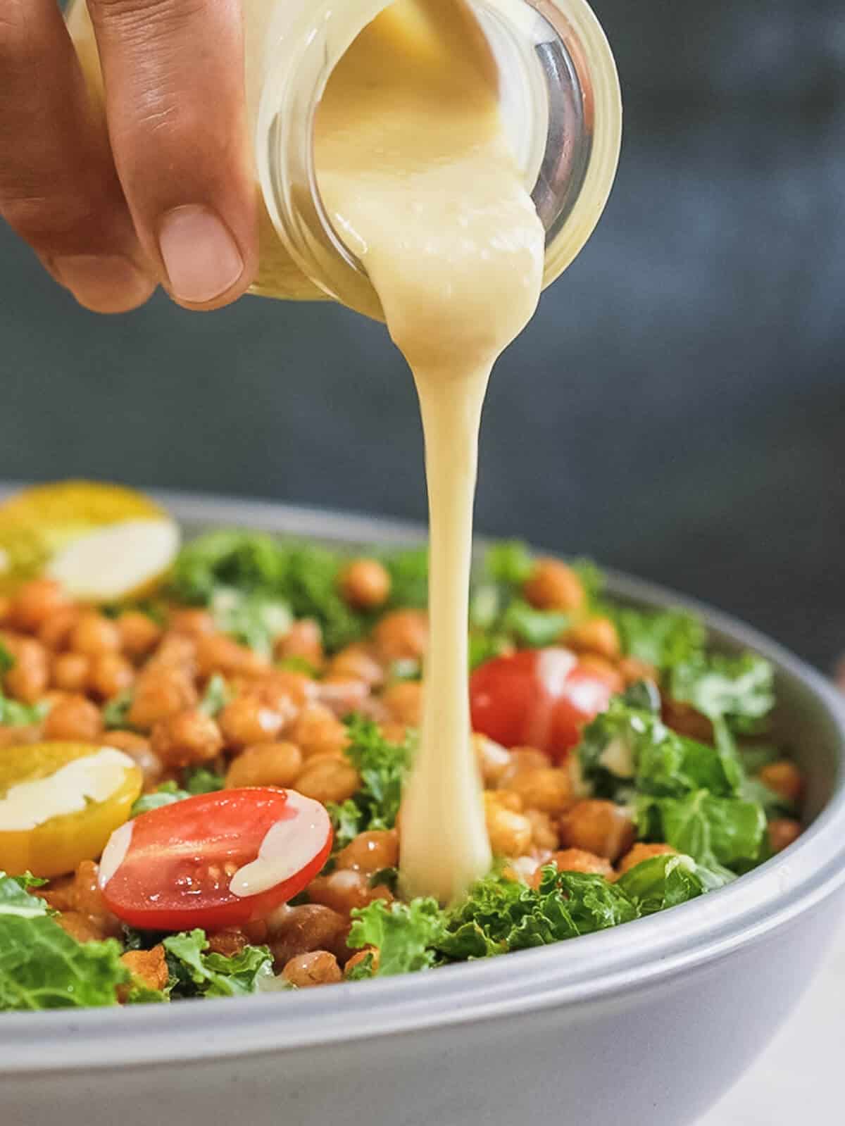 adding maple tahini sauce into a chickpea and kale salad.