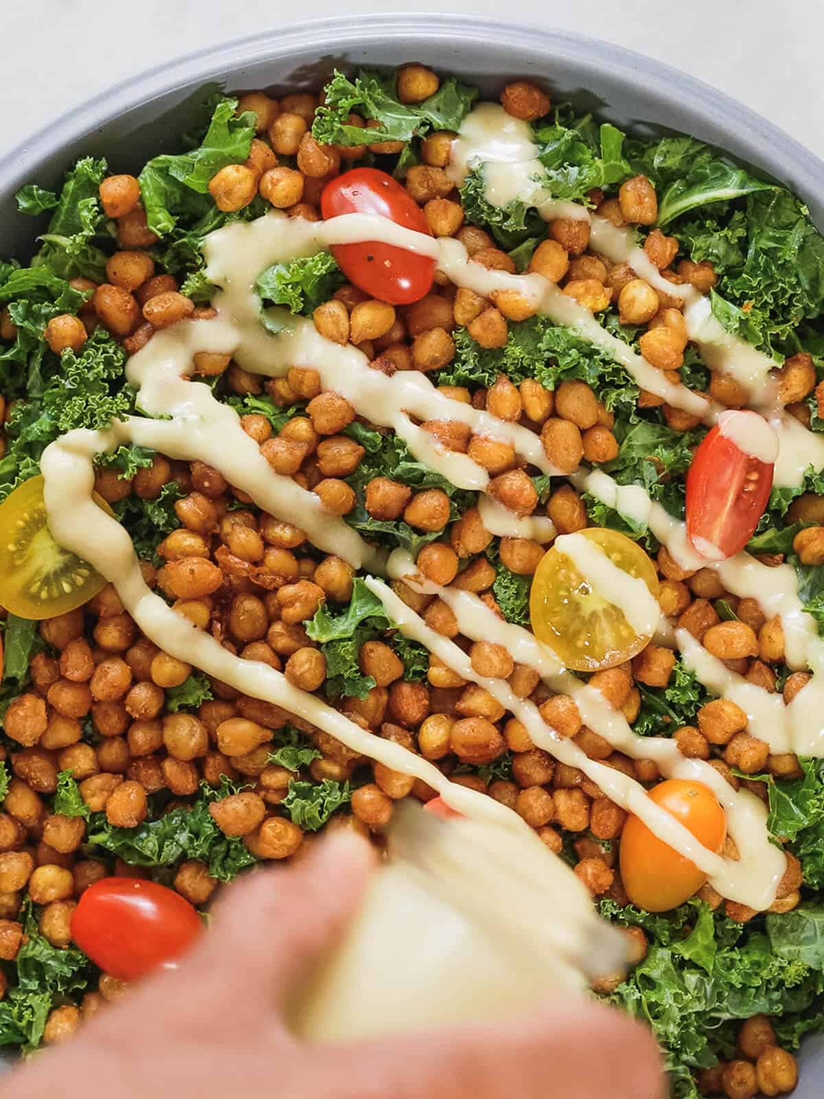 drizzling tahini dressing for kale salad over kale salad with crispy chickpeas.