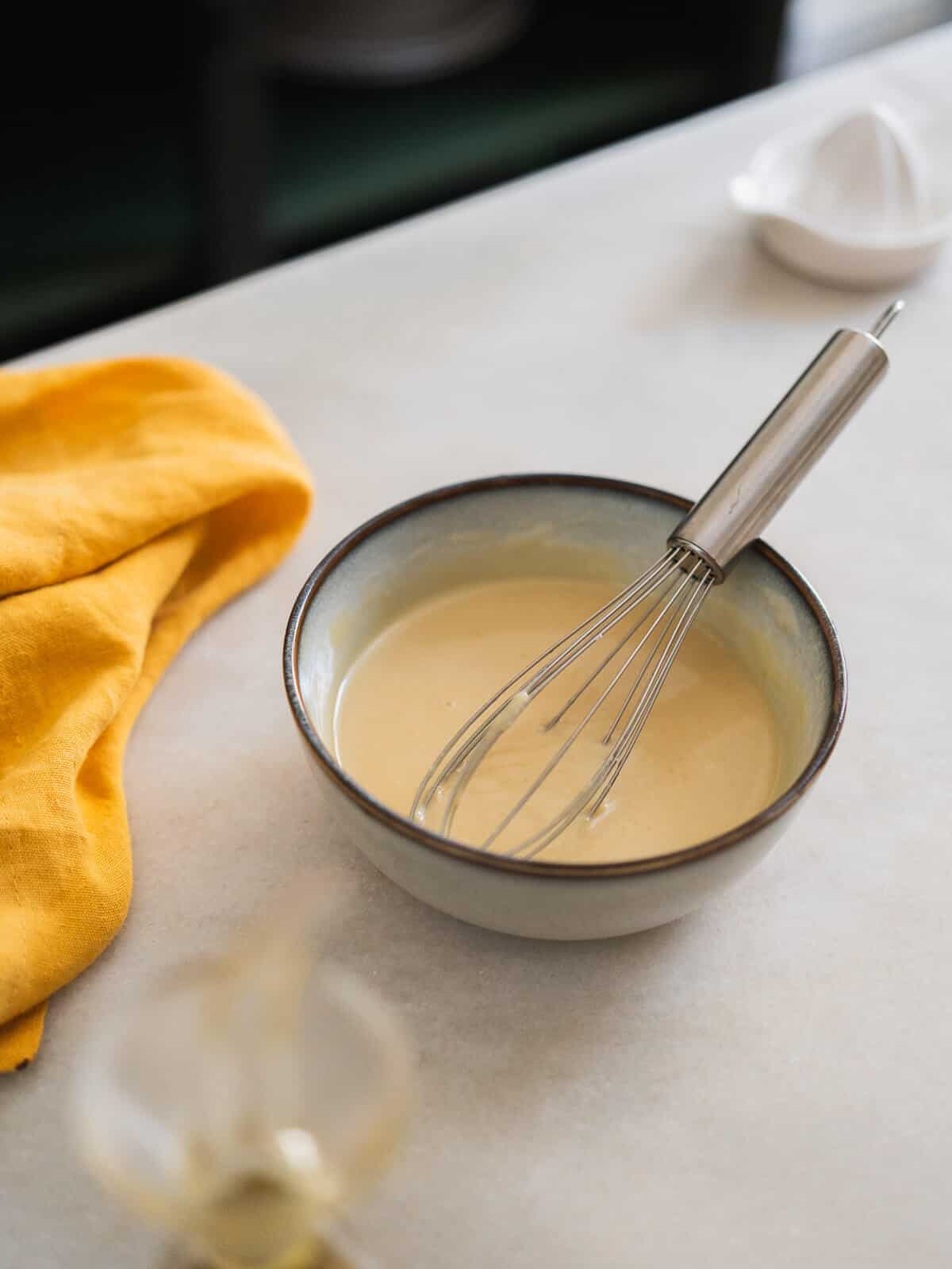 creamy textured maple tahini sauce in a bowl with a whisk.